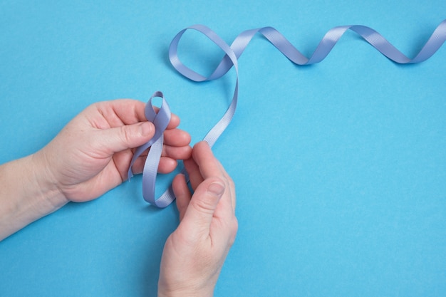 Grandmother and granddaughter hold a blue ribbon on a blue background, child's hands and woman's hands, copy space , diabetes and cancer symbol