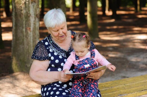 Photo grandmother and granddaughter reading the book in the park