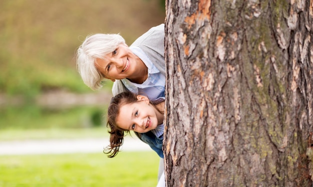 grandmother and granddaughter behind tree at park