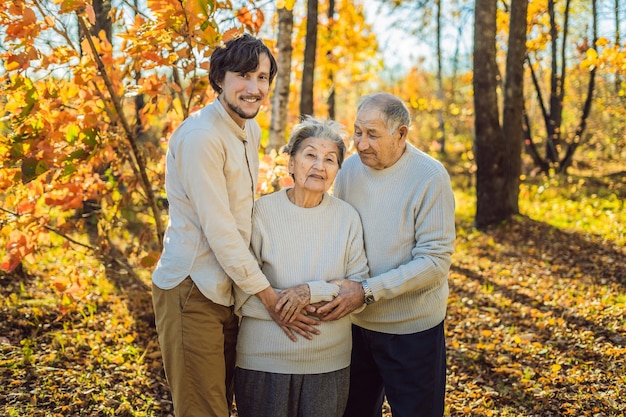 Grandmother grandfather and adult grandson hugging in autumn park