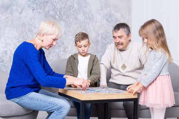 Бабушка, дедушка и внучка собирают пазлы за столом в гостиной. Семья проводит время вместе