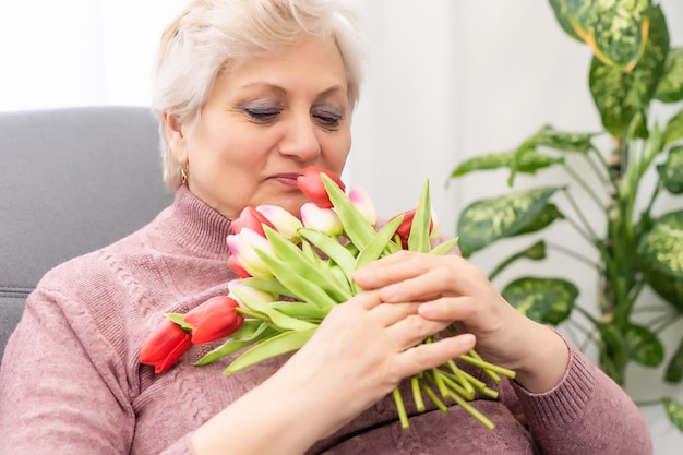 Бабушка держит букет цветов, улыбаясь.