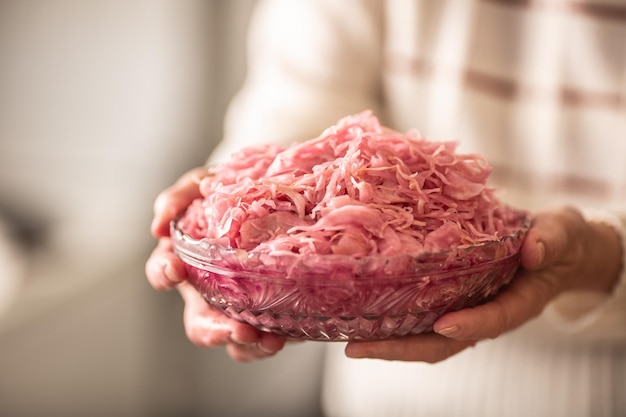 Grandmother holding in hands a glass bowl full of sour cabbage