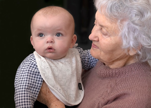 祖母は孫を抱きしめています。赤ちゃんを持つおばあさん。その少年は熱心に見守っていた。