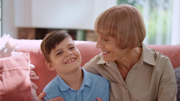 Grandmother hugging grandson in room Smiling boy talking with senior woman