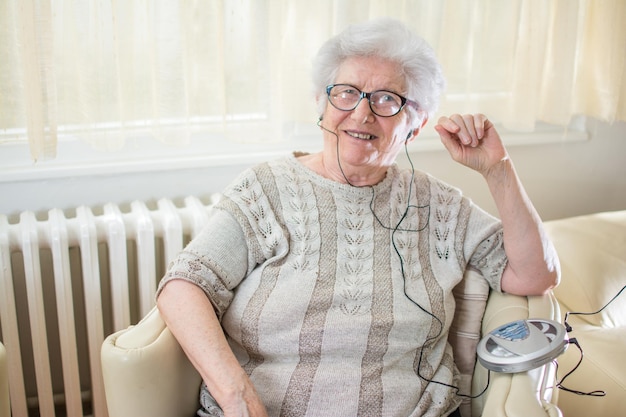 grandmother listening to music on cd player while sitting on armchair at home