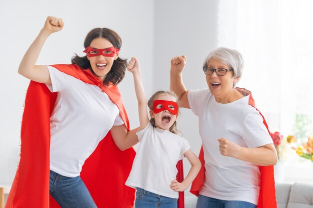 Grandmother mother and child playing together Girl and women in Superhero costumes