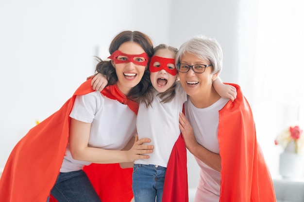 Grandmother mother and child playing together Girl and women in Superhero costumes