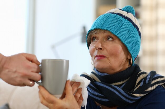 The grandmother sits on the couch and holds a cup