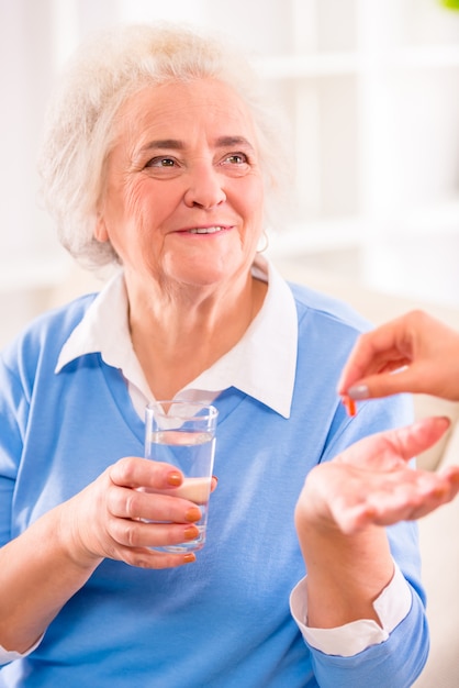 Grandmother sits and smiles holds a glass of water.