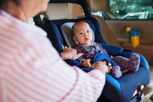 Grandmother takes care about her little granddaughter in a car, helps her and cheers up