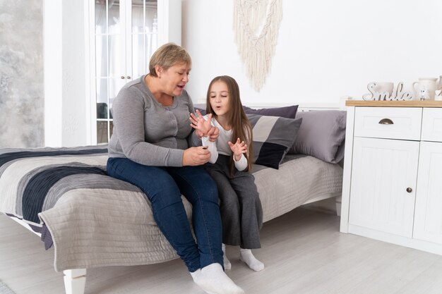 Grandmother and teen granddaughter sitting on the bed and doing manicure