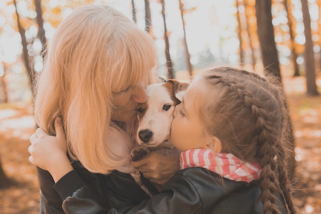 Foto nonna con la nipote in una ragazza del parco autunnale che abbraccia la nonna e il suo jack russell terrier