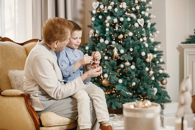 クリスマスの日に孫と祖母。クリスマス ツリーを飾る老婆と少年。ベージュとブルーの服を着た女性と男の子。