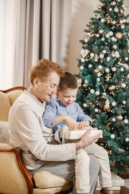 Grandmother with her grandson on Christmas day. Old woman and little boy opening a gift. Woman and boy wearing beige and blue clothes.