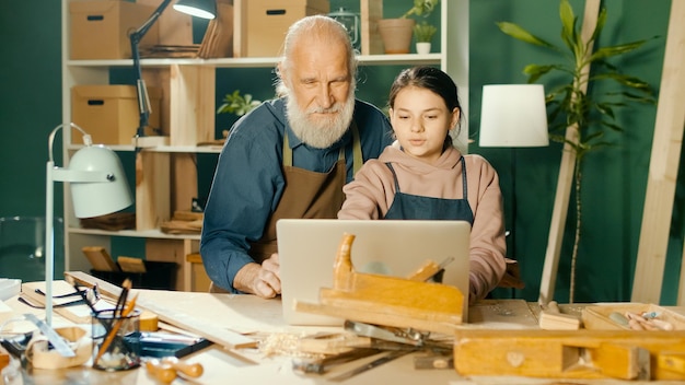 Photo grandpa carpenter with teenage granddaughter model 3d sketches using a laptop