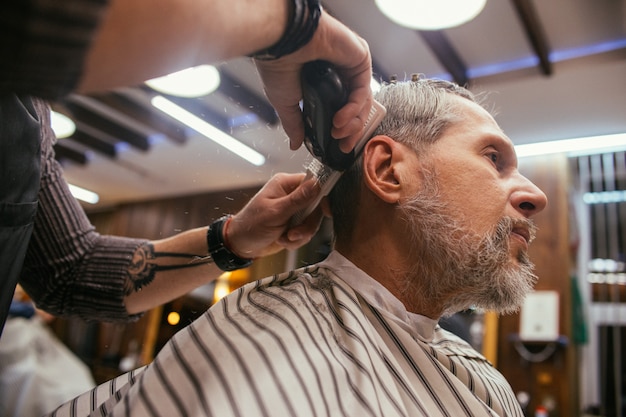 Дедушка подстригается в парикмахерской в парикмахерской. Модная стрижка пенсионера старика