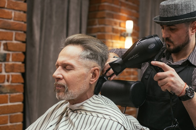 Taglio di capelli del nonno dal parrucchiere nel negozio di barbiere