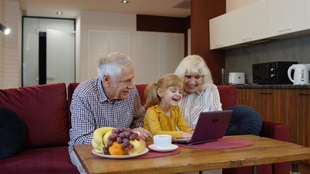 Photo grandparent with granddaughter using laptop at home