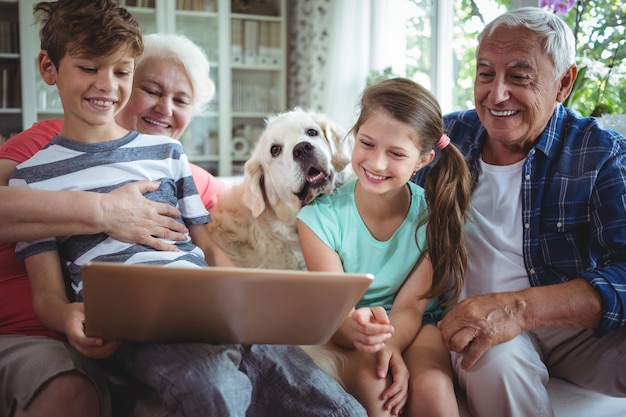 Photo grandparents and grandchildren using laptop in living room