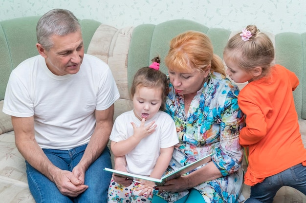 grandparents and granddaughters sitting on the couch reading a book