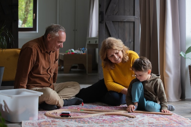 Grandparents play the railway with their grandson at home.