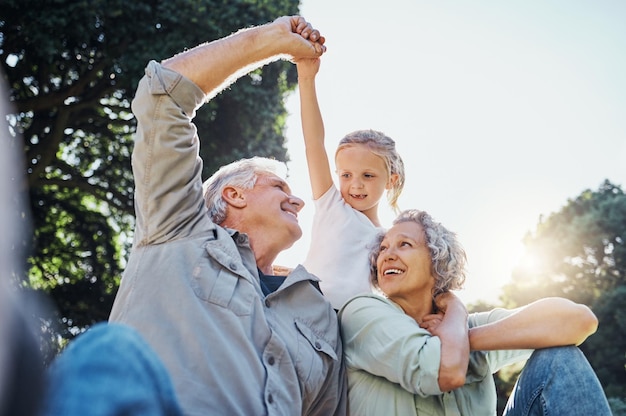 Grandparents playing together with a girl in the park in the morning Family love and grandchild bonding with grandmother and grandmother in a garden Child holding hands with senior couple outside