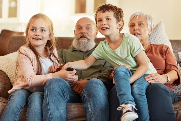 写真 家のリビングルームで祖父母のテレビと子供たちが一緒にウェブシリーズをストリーミングしている高齢者の子供とテレビのリモコンが家のラウンジソファで子供の映画や映画と一緒にビデオを見ている