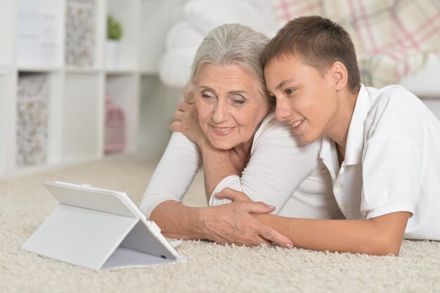 Nipote con la nonna che guarda il tablet sdraiato sul pavimento