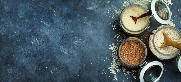 Granen (havermout, boekweit, rijst) in glazen potten op de achtergrond van de keukenbanner. Glutenvrij concept. Soorten granen voor het maken van gezonde zelfgemaakte gerechten en maaltijden.