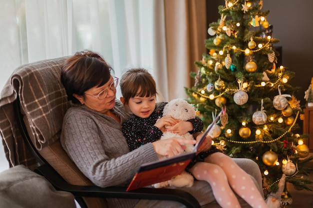 おばあちゃんと孫娘がクリスマス ツリーの近くで本を読んで