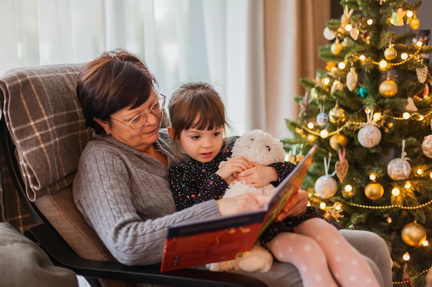 Granny and granddaughter reading a book near the Christmas tree