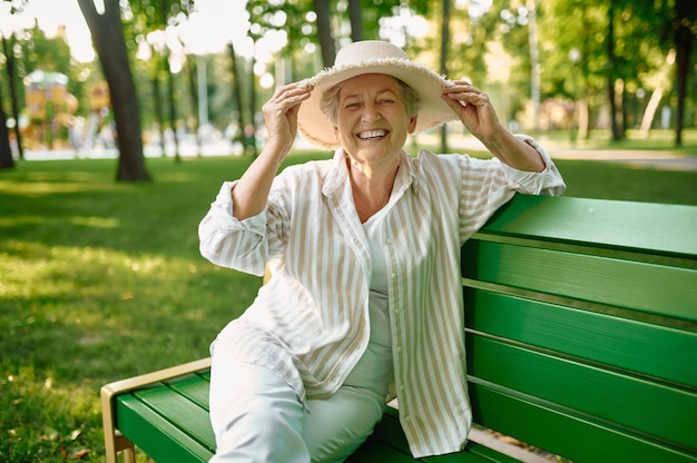 Granny in hat sitting on the bench in summer park