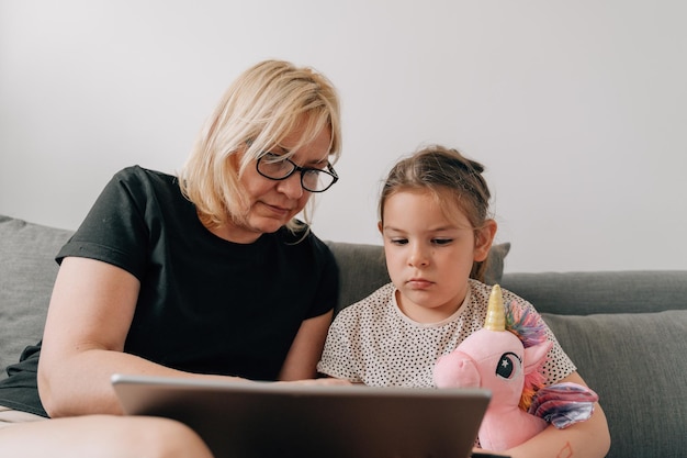 Granny and preschool girl using tablet together at home on the sofa family togetherness time