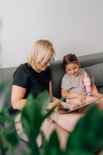 Granny and preschool girl using tablet together at home on the sofa family togetherness time