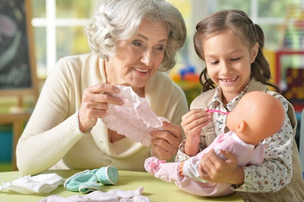 Granny with granddaughter playing together with baby doll