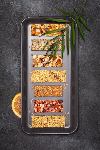 Granola bars with nuts seeds oats berries dry fruits and palm leaf on textured black background