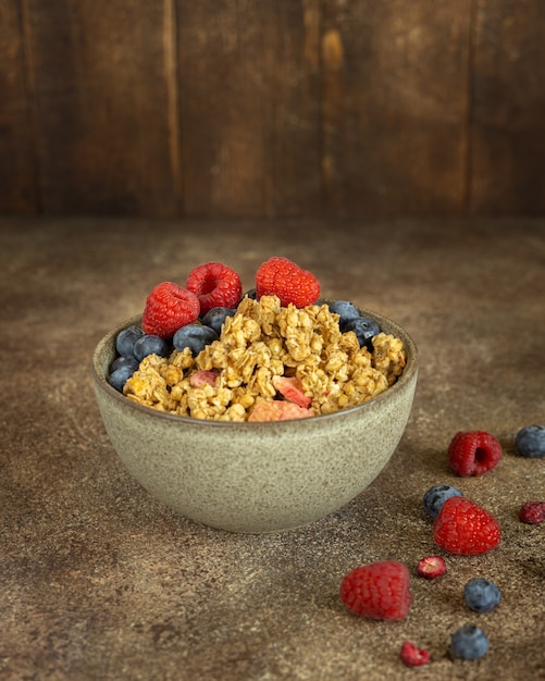 Granola bowl with strawberry and blueberry on the brown rustic wooden background, summer superfood breakfast concept