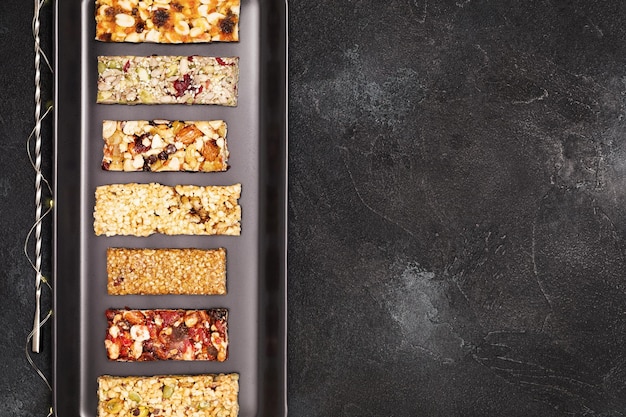 Photo granola cereal bars with nuts seeds oats berries and dry fruits on black background with copy space