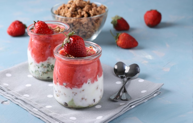 Granola crispy with strawberry spinach and natural yogurt in glass jars on light blue background