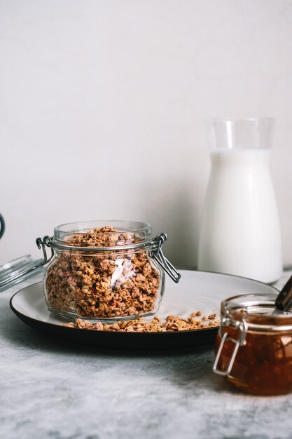 Granola in glass jar and carafe of milk on a table.