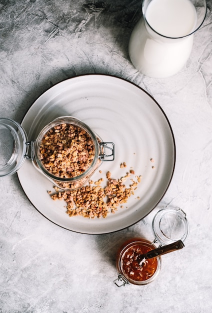 Granola in glass jar and carafe of milk on a table.