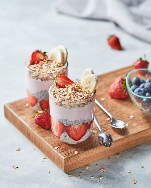 Granola helften van aardbeien banaan chia zaden met yoghurt in een bril op een houten bord op een