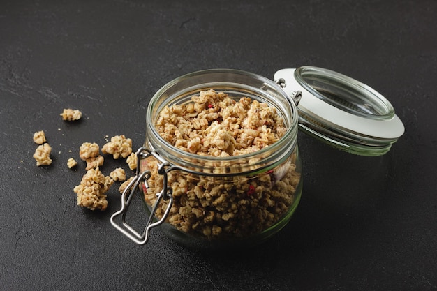 Granola in pot. Gezond zelfgemaakt ontbijt op zwarte tafel. Zijaanzicht eten.