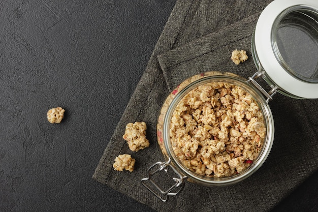 Granola in pot op donker servet. Gezonde voeding op zwarte tafel. Bovenaanzicht.