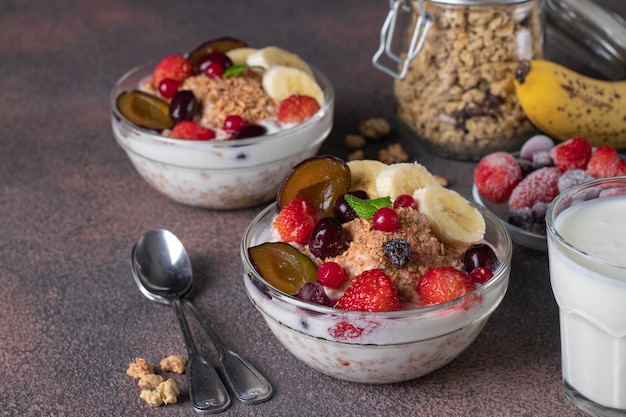 Granola knapperige muesli met natuurlijke yoghurt bevroren bessen en fruit en noten in twee glazen kommen op bruine achtergrond