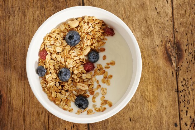 Granola met yoghurt en bessen in een witte kom op een houten tafel