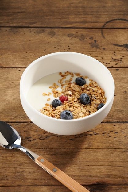 Granola met yoghurt en bessen in een witte kom op een houten tafel