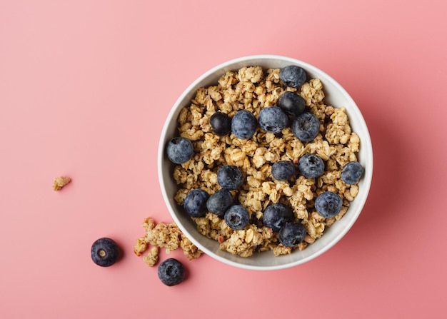 Granola with blueberry in bowl on pink background Healthy food Top view