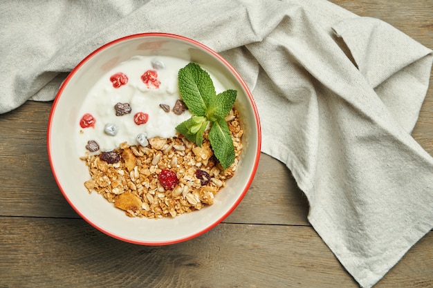 Photo granola with greek yogurt and berries in a bowl with linen cloth on a wooden surface. close up with place for text. classic breakfast